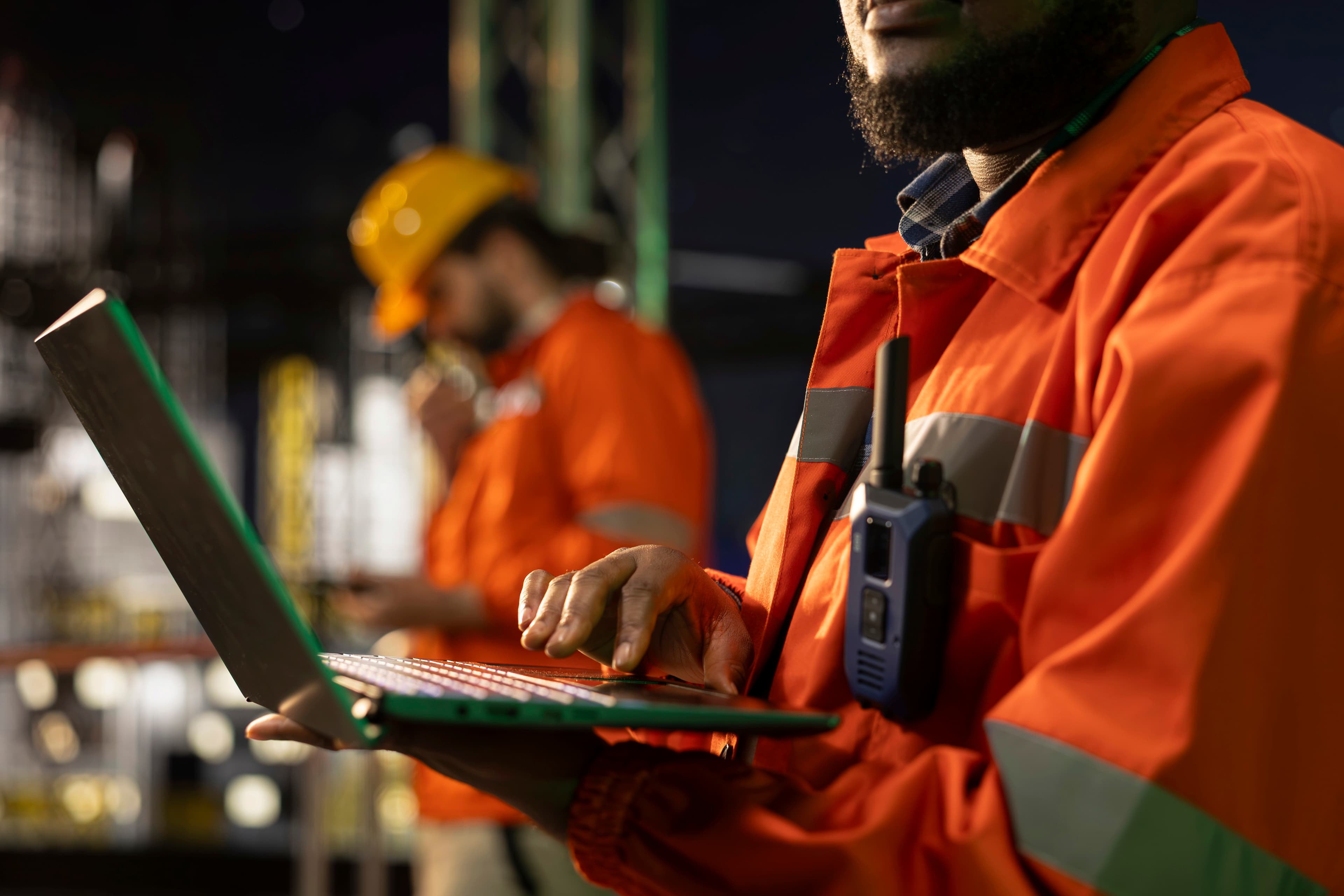 Técnico Nexo com laptop e walkie-talkie em obra elétrica industrial noturna